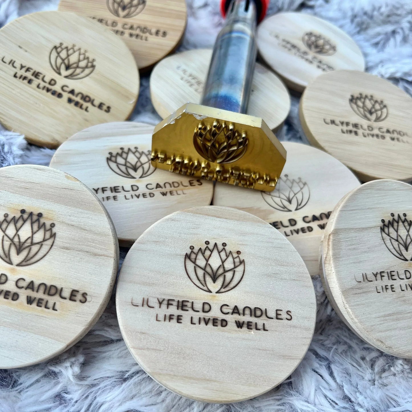 Wooden candle lids stamped with Lilyfield Candles logo and embossing tool on soft fabric