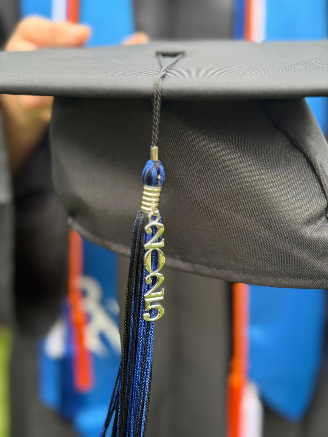 Black graduation cap with 2025 tassel, blue and orange graduation stole in background