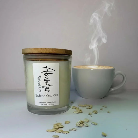 Spiced oat milk candle with bamboo lid, cup of latte, and oat flakes on white table