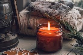Cozy candle in glass jar with wool sweater, lantern, and pine branches, rustic winter decor