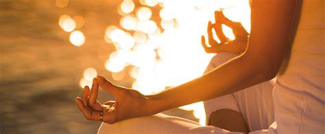 Person meditating outdoors by water at sunset, practicing yoga with relaxed hands