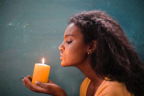 Woman blowing out yellow candle against teal background, close-up, relaxation concept