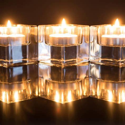Three tealight candles in clear glass holders glowing on a reflective surface