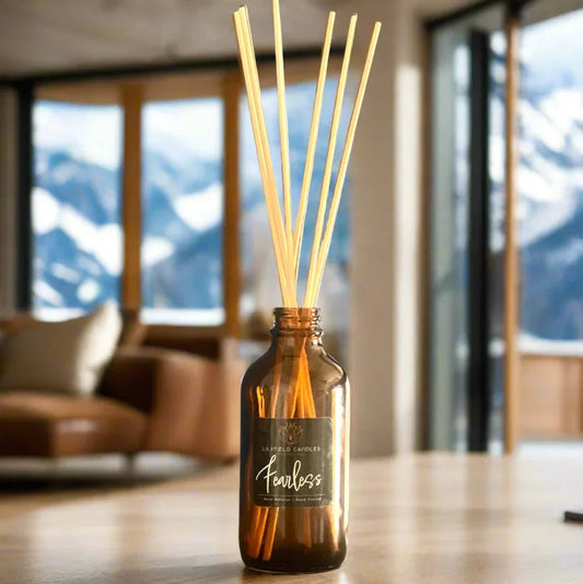 Amber glass reed diffuser with 'fearless' label on wood table, cozy living room, mountain view