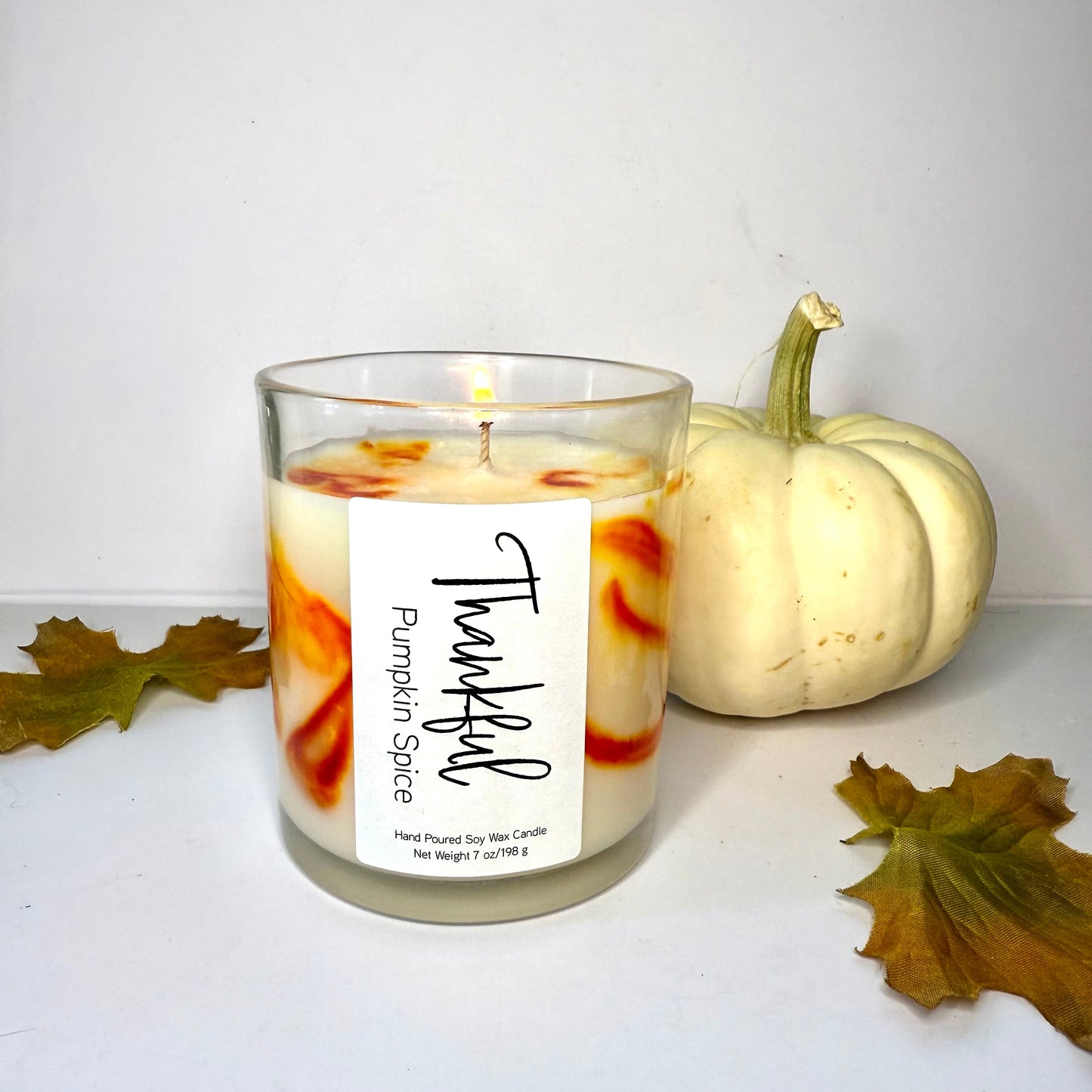 Candle labeled 'Pumpkin Spice' with a white pumpkin and leaves on a light background